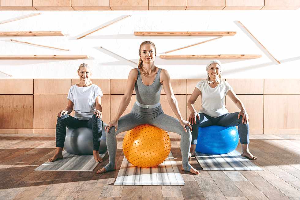 two mature woman with their sports teacher sitting on fitball