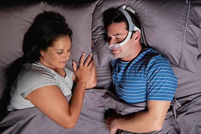 Couple is sleeping in bed and he is wearing a breathing mask